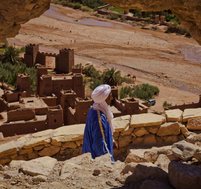A man in the Sahara Desert wearing traditional, lightweight desert clothing suited for the hot, sunny environment, standing amid sand dunes under a clear sky