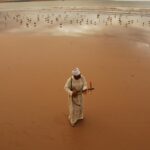 A man playing a traditional musical instrument amid the sand dunes of Merzouga in the Sahara Desert.
