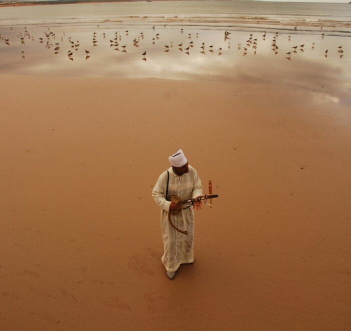 A man playing a traditional musical instrument amid the sand dunes of Merzouga in the Sahara Desert.