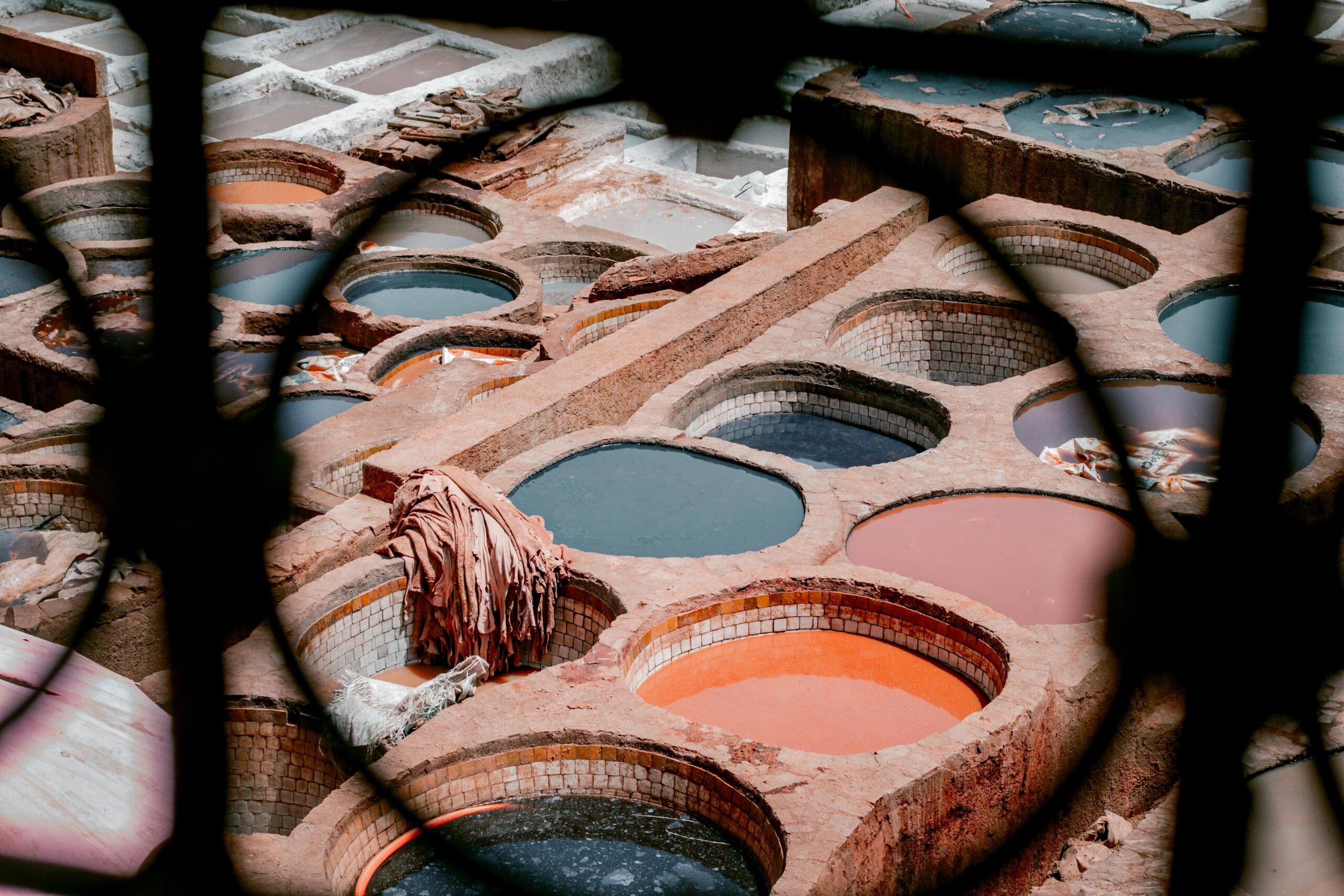 Overhead view of the Chouara Tanneries in Fes, Morocco, showing colorful dyeing vats surrounded by traditional stone buildings where leather is processed by skilled artisans.