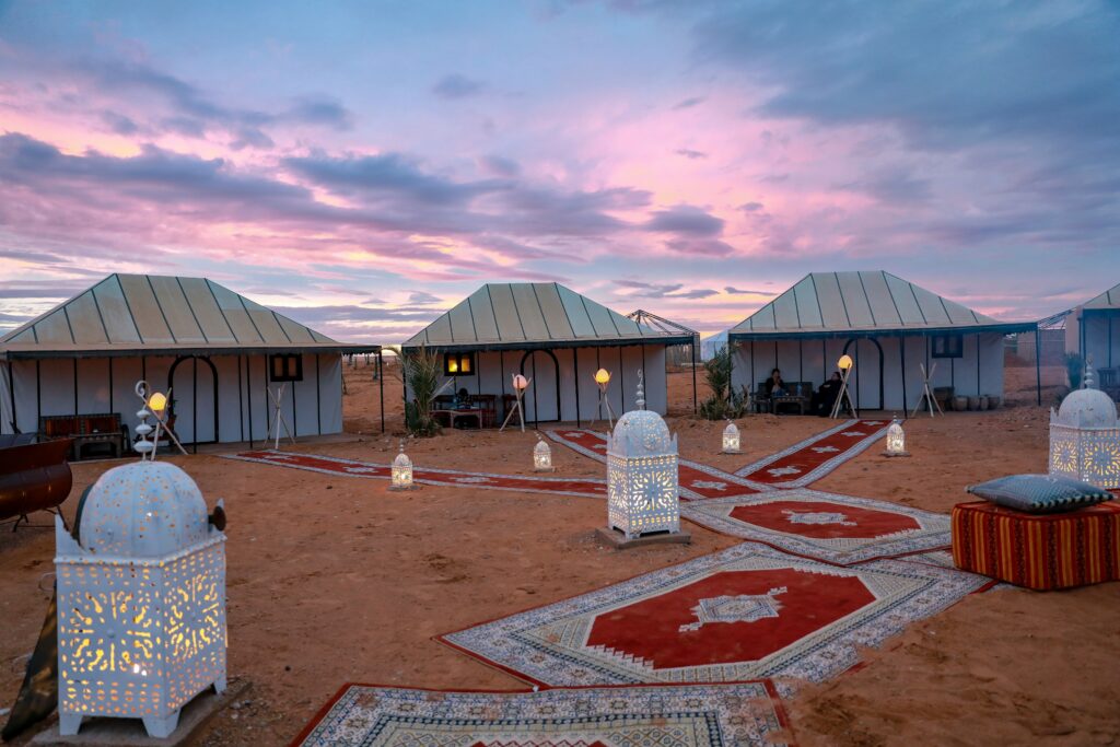 A cluster of traditional desert tents set up in the vast golden sands of the Moroccan Sahara under a clear blue sky, capturing the serene and remote beauty of the desert landscape.